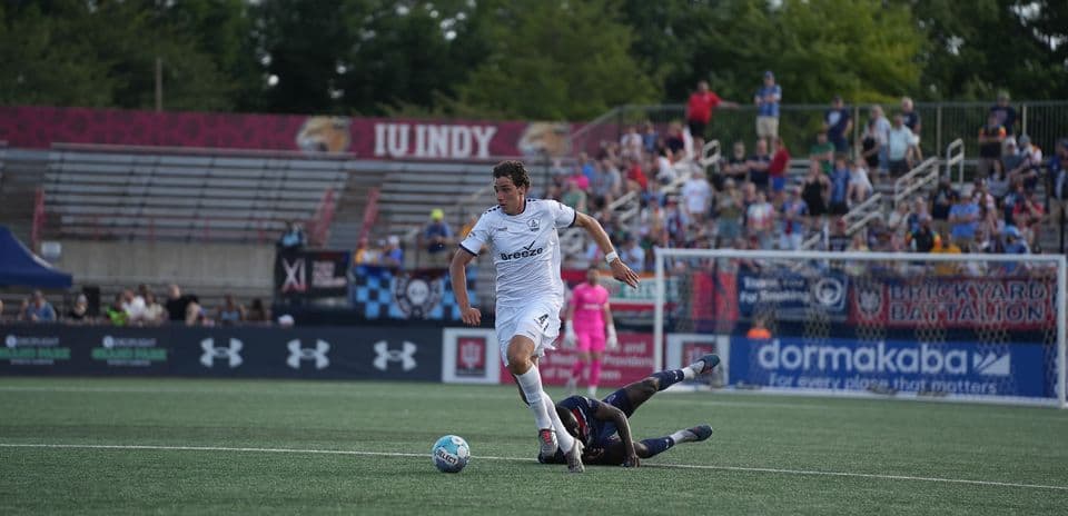 Jugador de Rhode Island driblando a oponente caído