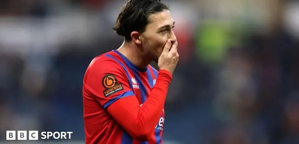 Jugador con camiseta roja tocándose la cara en el campo
