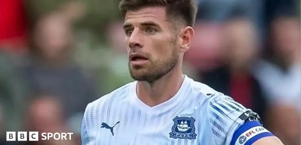 Jugador con camiseta blanca y brazalete en el campo