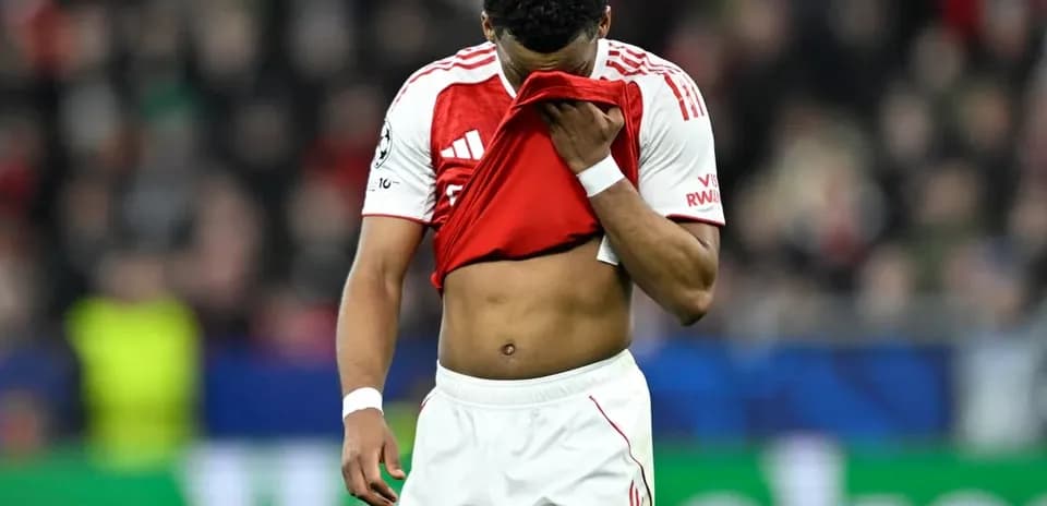 Jugador con camiseta roja cubriendo su rostro en el campo