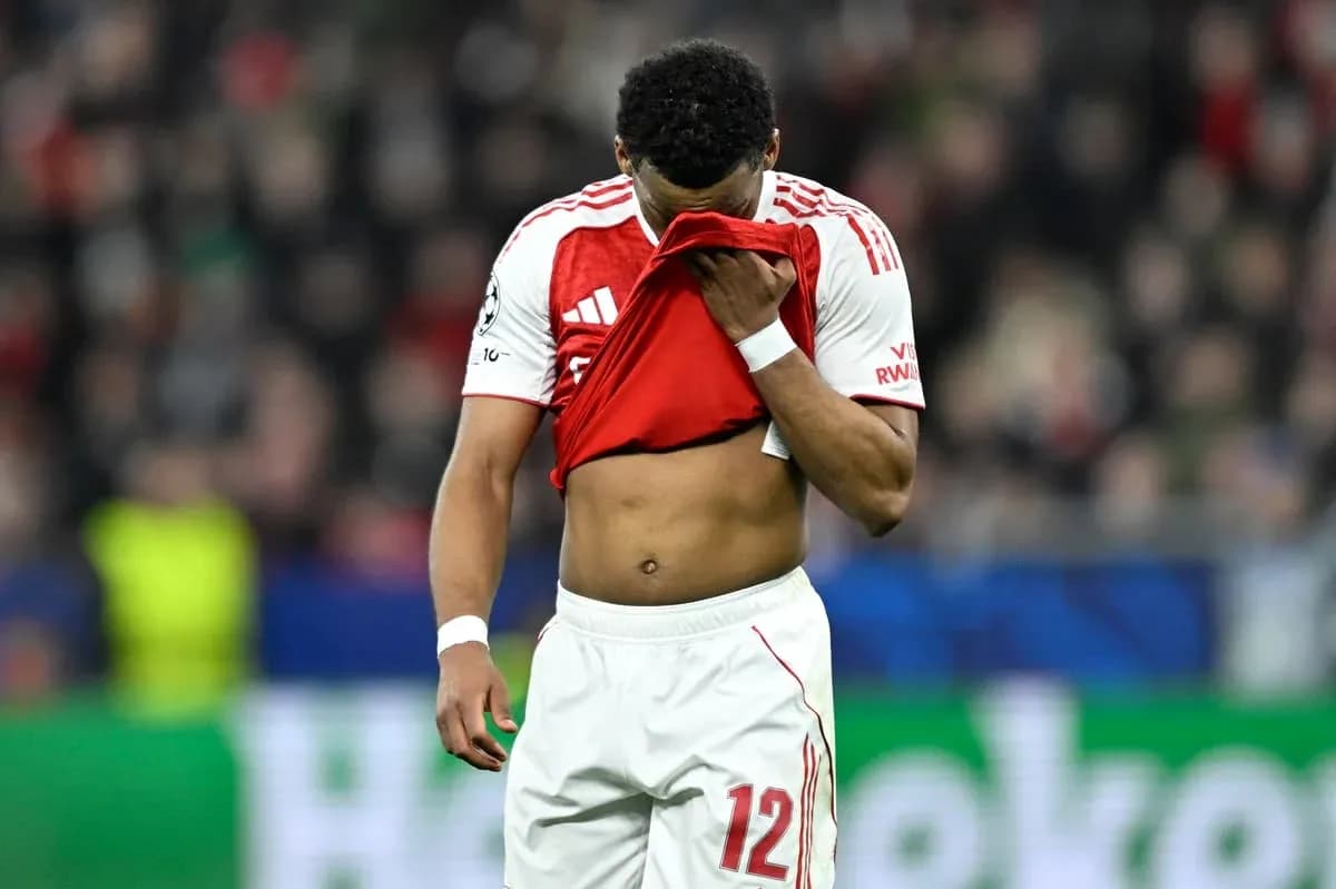 Jugador con camiseta roja cubriendo su rostro en el campo