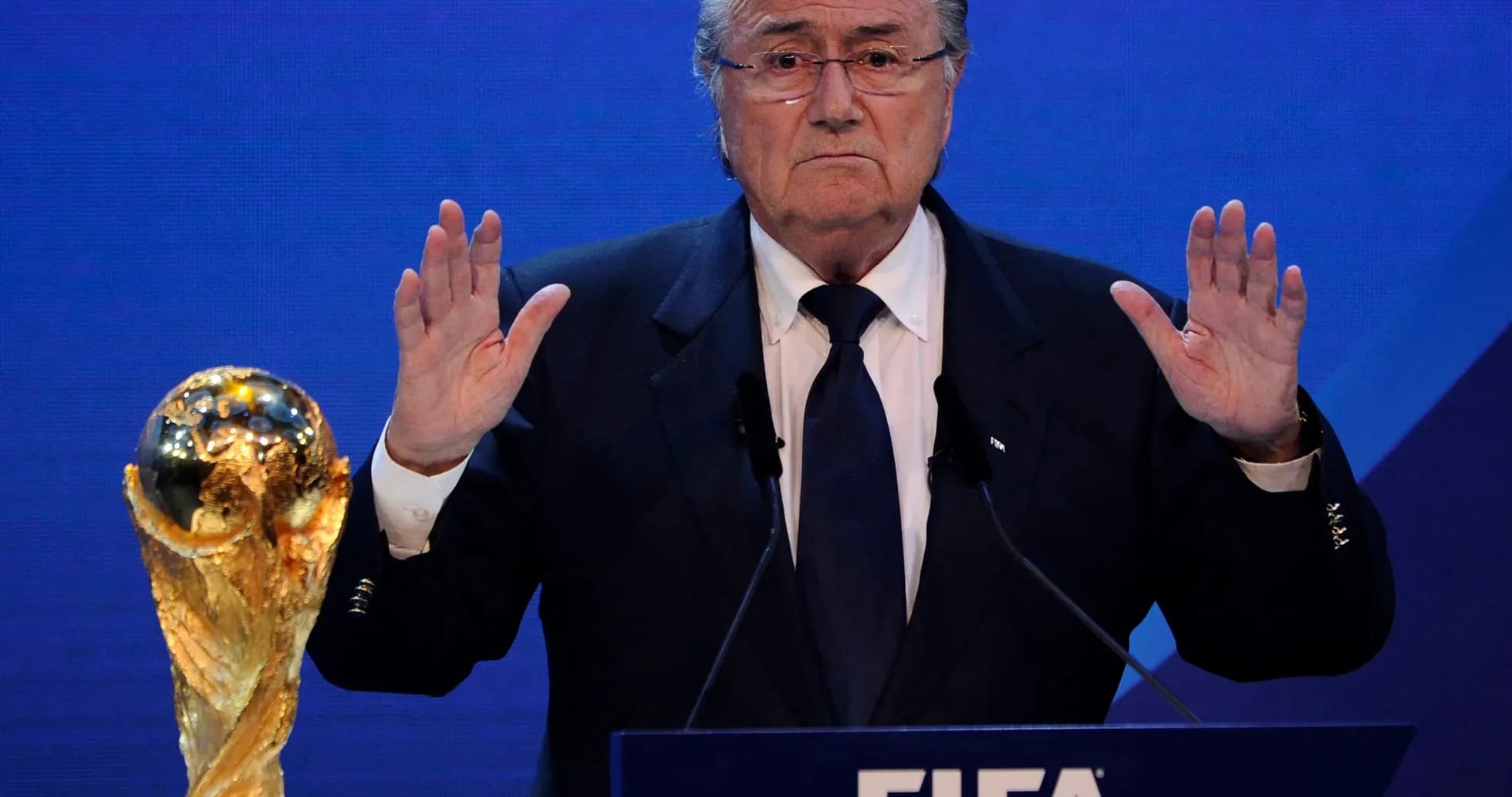 Hombre hablando en conferencia con trofeo de la FIFA