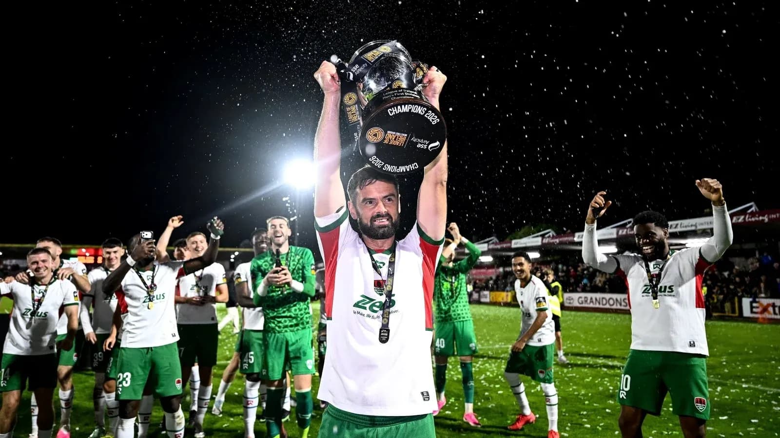 Jugador levantando trofeo con equipo celebrando detrás