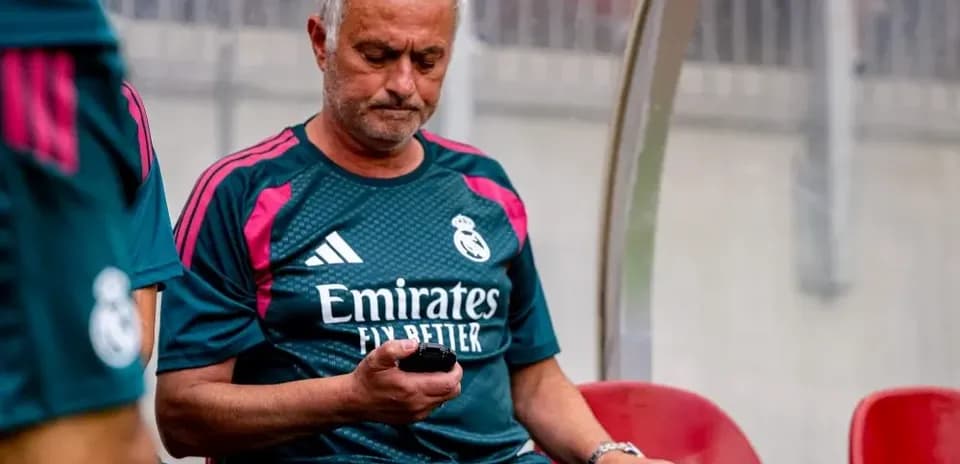 Entrenador de Real Madrid revisando su teléfono en banquillo