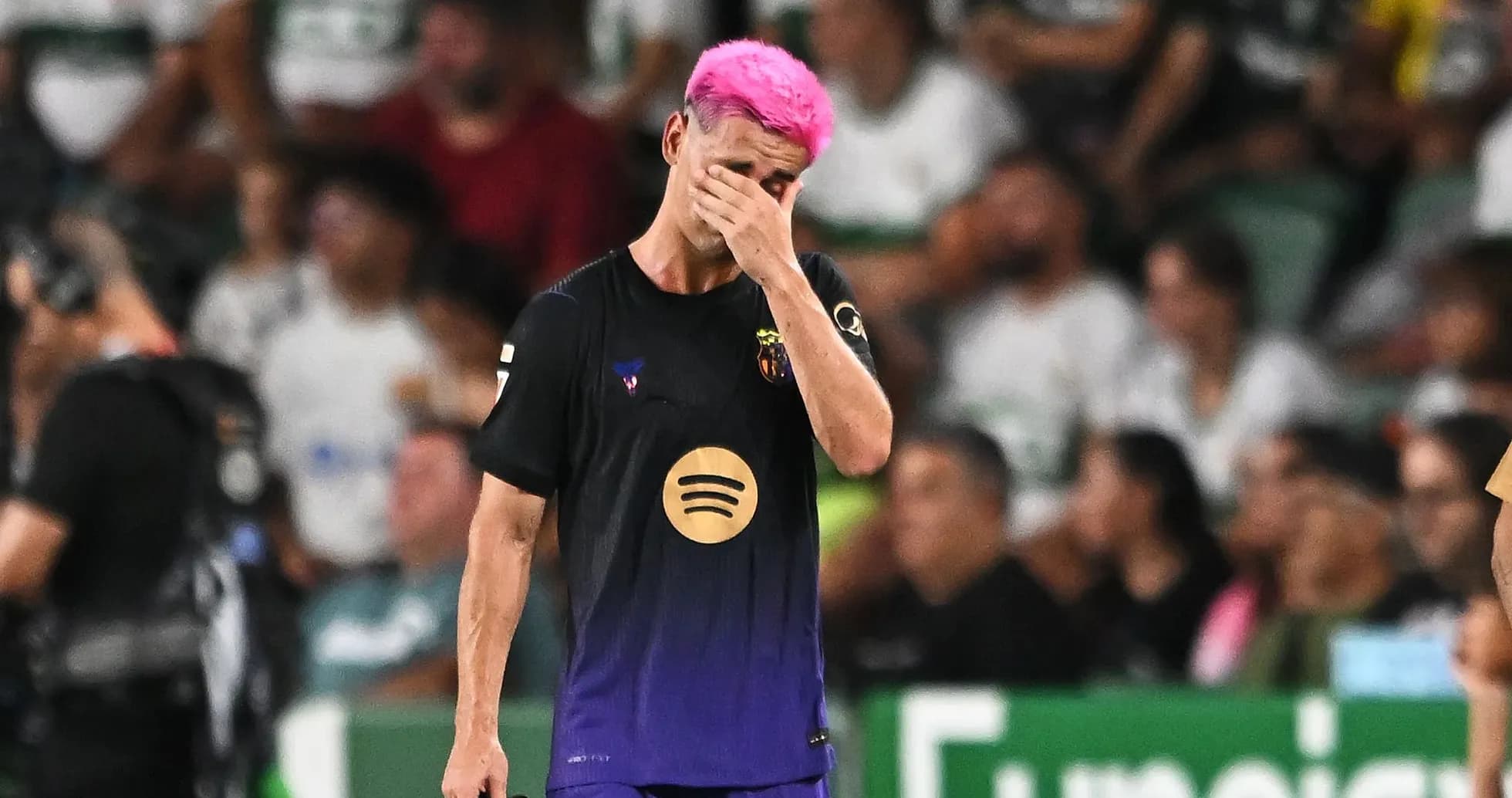 Jugador con cabello rosa cubriéndose la cara en el campo