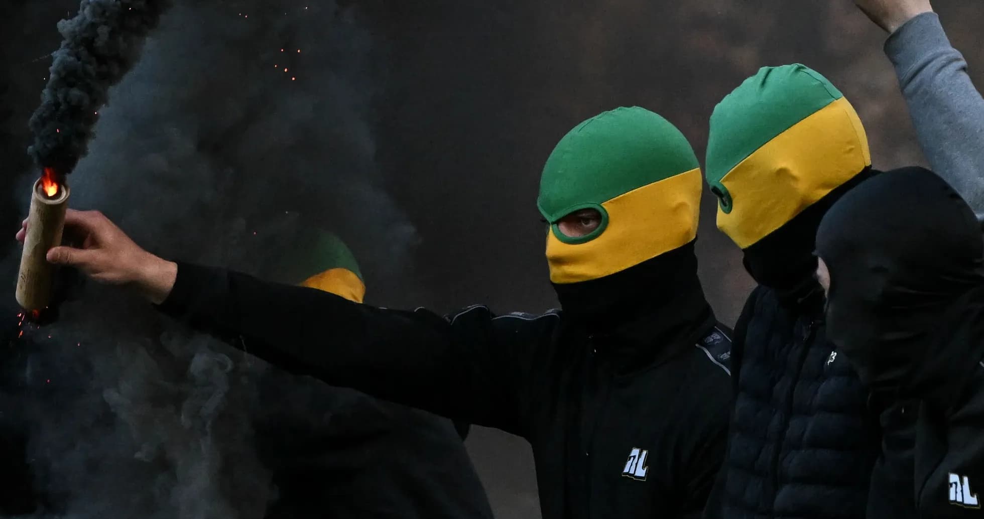 Grupo de personas con máscaras y bengalas encendidas