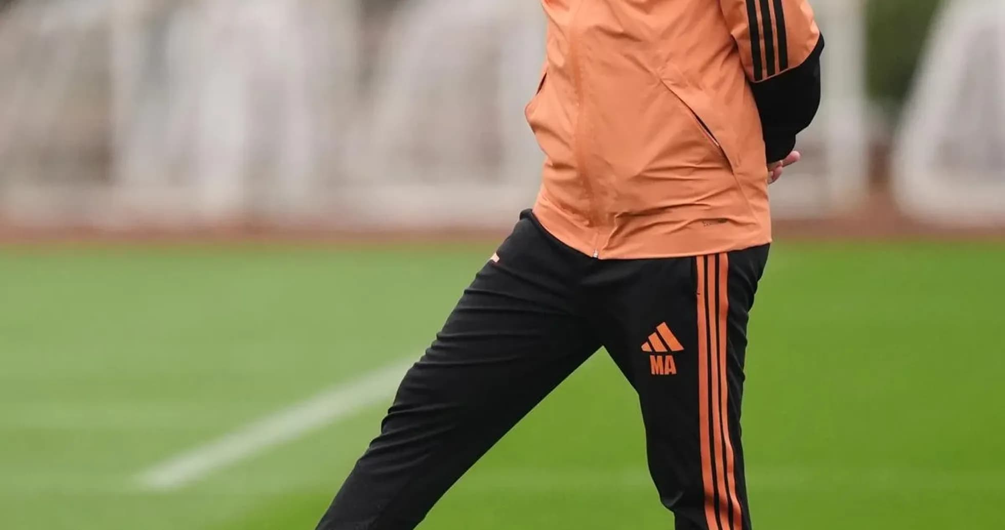 Entrenador de pie con balón en el campo de entrenamiento