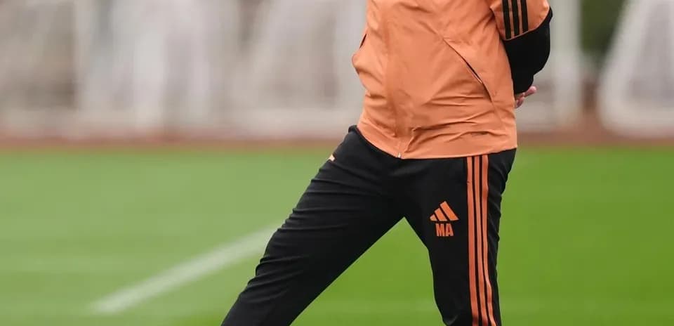 Entrenador de pie con balón en el campo de entrenamiento