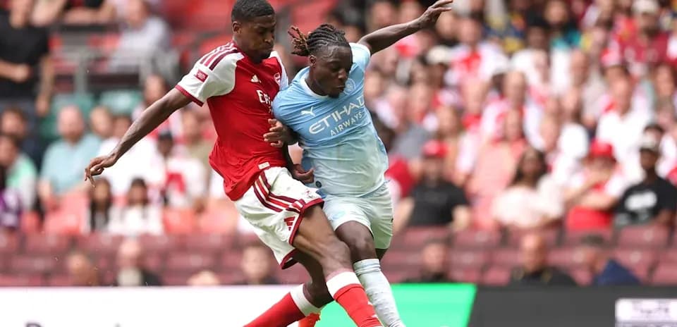 Jugador de Arsenal compitiendo por el balón con jugador de Manchester City