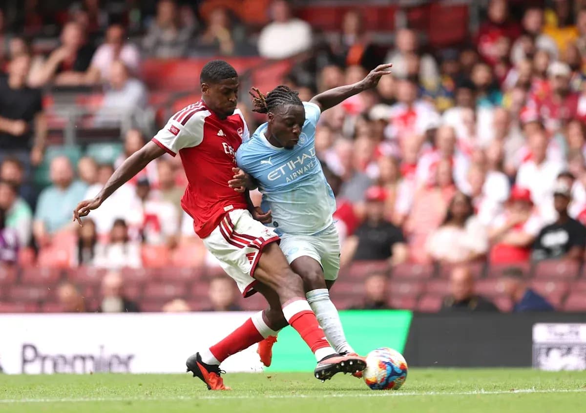 Jugador de Arsenal compitiendo por el balón con jugador de Manchester City