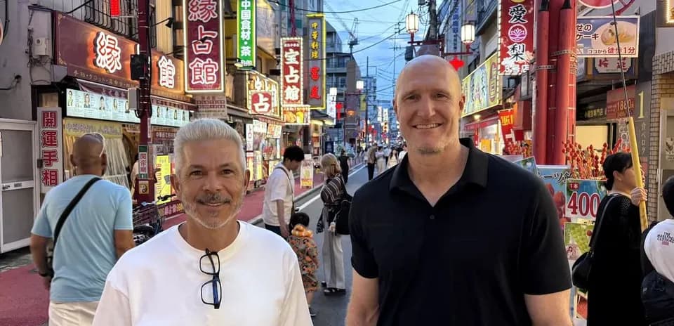 Dos hombres sonriendo en calle iluminada de Tokio