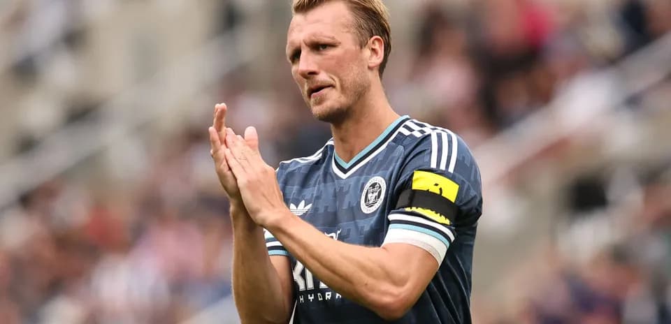 Jugador aplaudiendo con banda de capitán en el campo