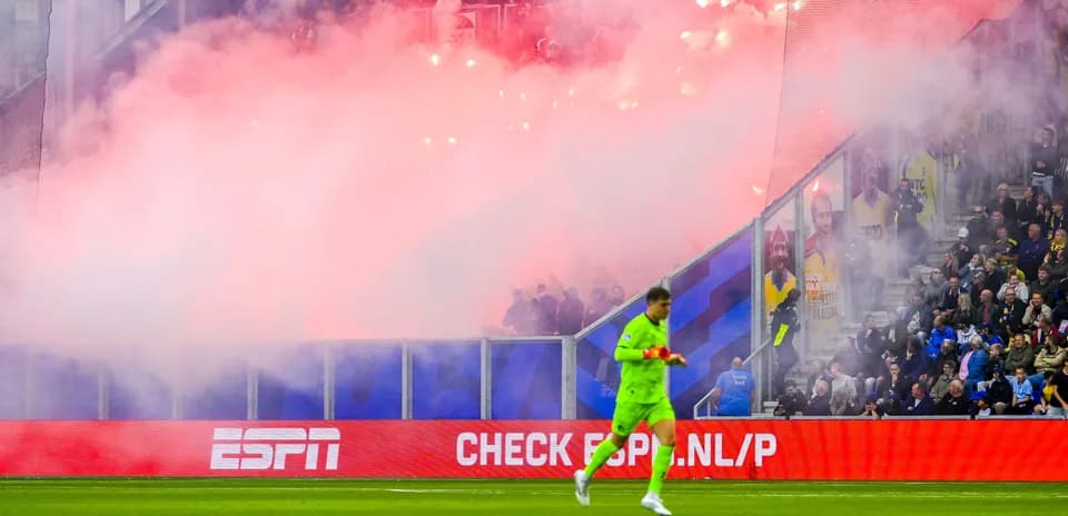 Portero caminando frente a hinchas con pirotecnia