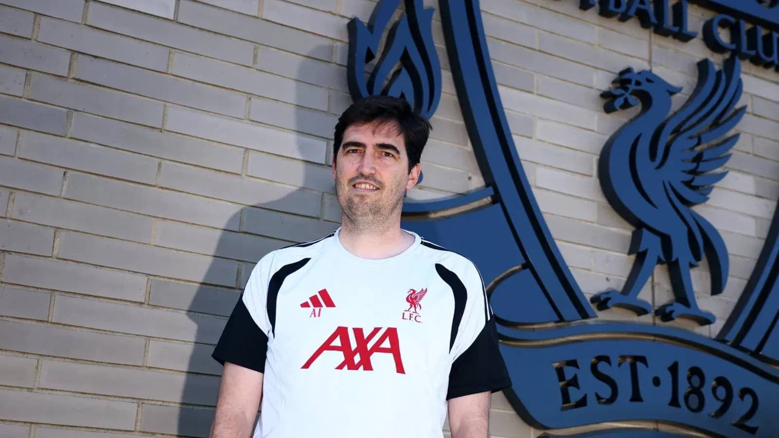 Entrenador posando frente al escudo del Liverpool