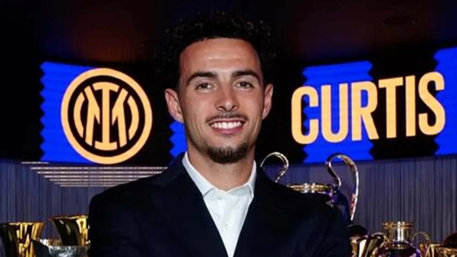 Jugador sonriente junto a trofeos y logo del club